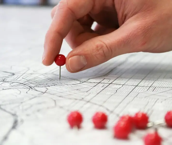 Hand placing red pins on a paper map